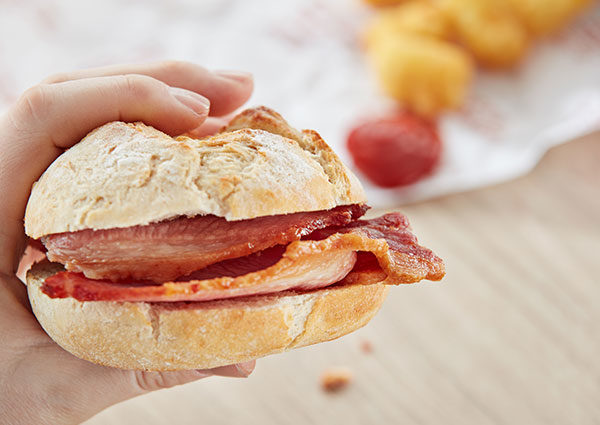 Hand holding bacon sandwich - food-to-go from a Flexeserve heated display