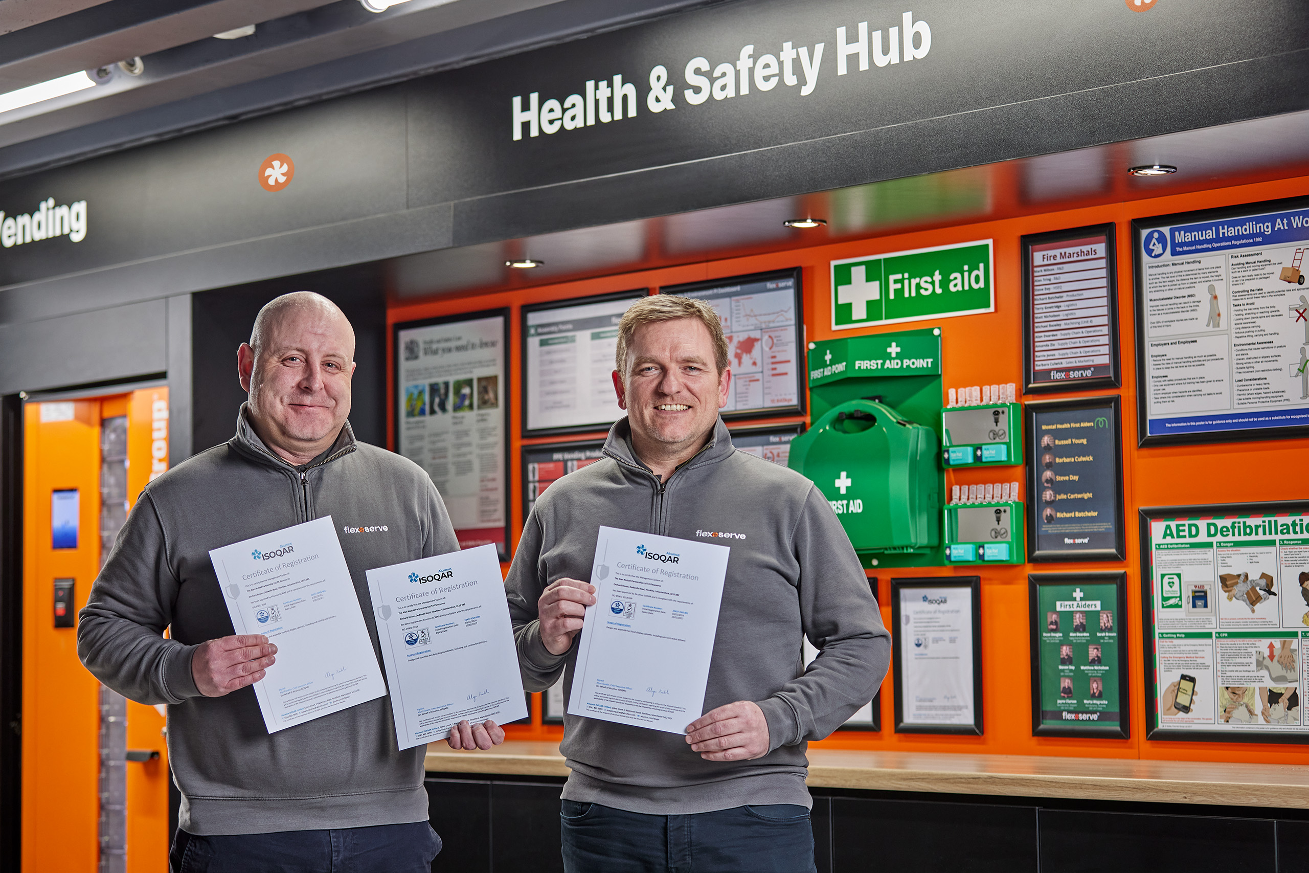 [L-R] Anthony Stubbs, HSEQ Manager and Mark Manley, Director of Manufacturing Operations pictured next to the Flexeserve Health & Safety Hub with ISO certifications 9001, 14001 and 45001